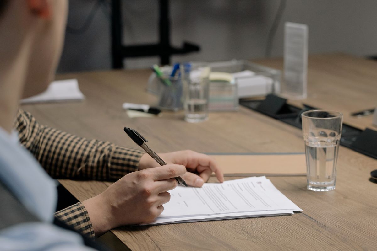 A person at a meeting table holding a pen over a document, about to put a complaint in writing