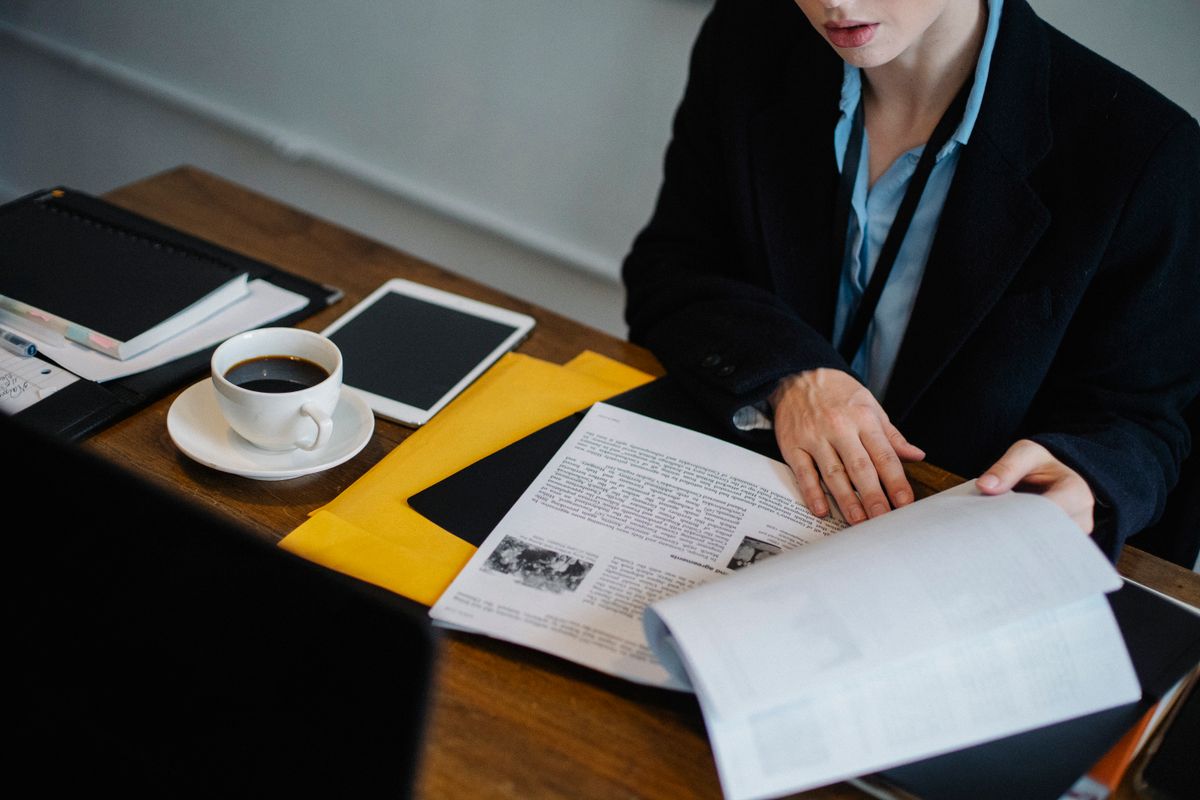 A professional at a desk working through paperwork, with a tablet, notebook and coffee alongside